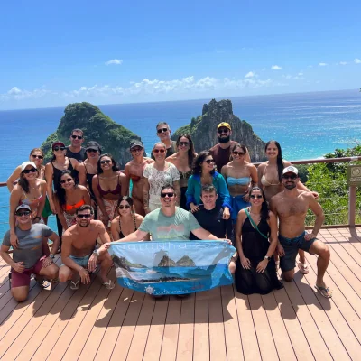 Grupo de viajantes em um mirante de Noronha, com o Morro Dois Irmãos ao fundo