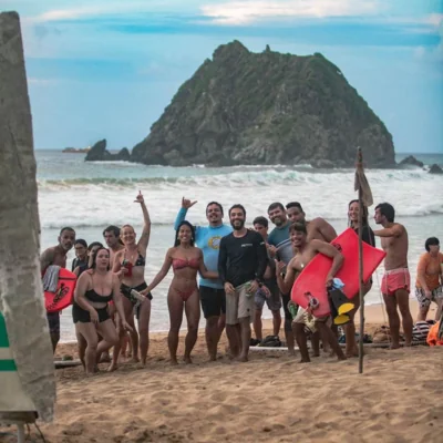 Grupo reunido na areia, com pranchas e a paisagem de Noronha